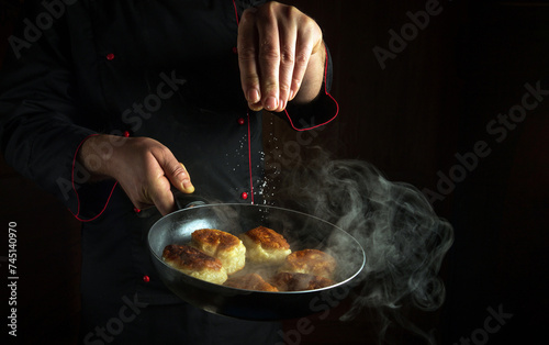 Fototapeta Naklejka Na Ścianę i Meble -  Professional chef adds salt to pancakes in a hot frying pan. The concept of preparing a delicious Ukrainian national dish or pancakes in the kitchen of a public house. Black space for recipe or menu.