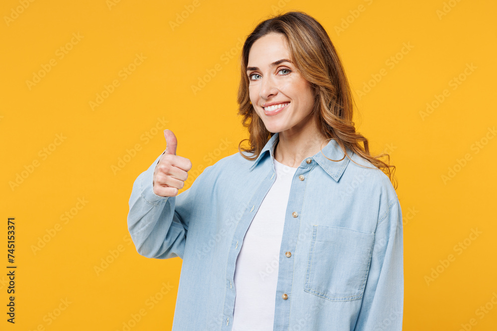 Young smiling happy satisfied cheerful fun woman she wear blue shirt white t-shirt casual clothes showing thumb up like gesture isolated on plain yellow background studio portrait. Lifestyle concept.