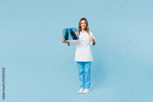 Full body female doctor woman wear medical gown suit work in hospital clinic hold roentgen X-ray of lungs with pneumonia show thumb up isolated on plain blue background. Health care medicine concept. photo