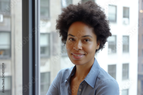 Afro woman smiling stands against window with blurred cityscape