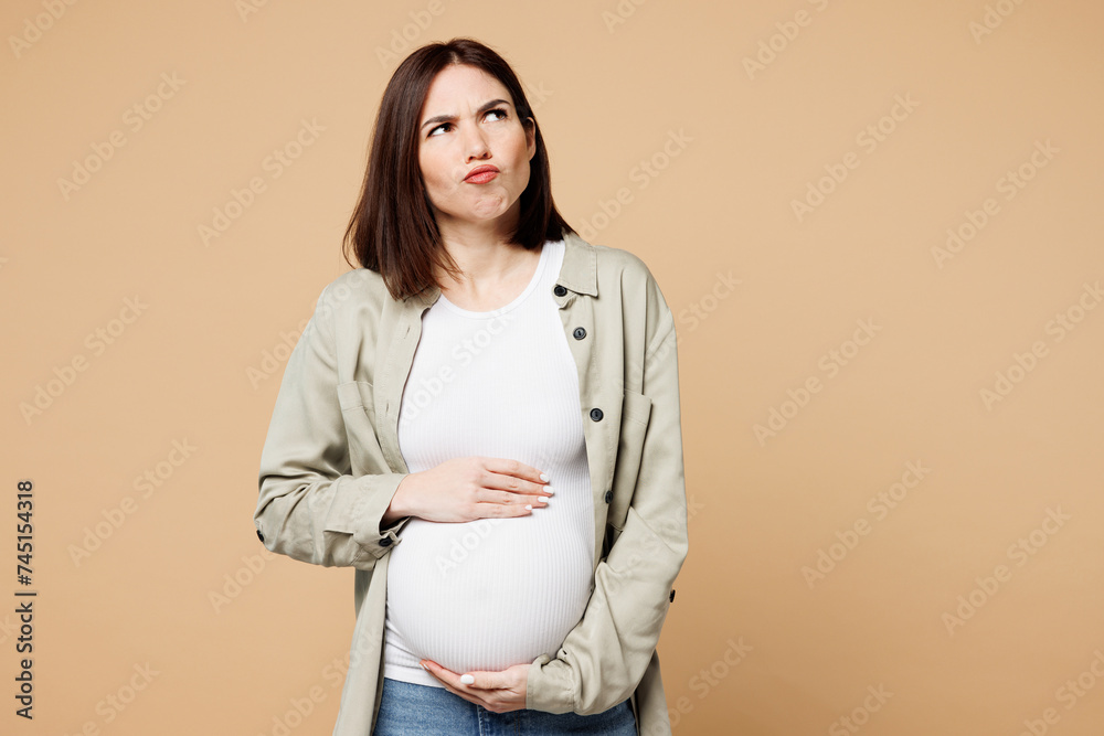 Young minded sad upset pregnant expectant woman future mom wear grey shirt with belly stomach tummy with baby look aside on area isolated on plain beige background. Maternity family pregnancy concept. Young minded sad upset pregnant expectant woman future mom wear grey shirt with belly stomach tummy with baby look aside on area isolated on plain beige background. Maternity family pregnancy concept.