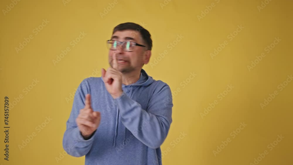 Senior man with glasses on a yellow background asking for silence Senior man with glasses on a yellow background asking for silence