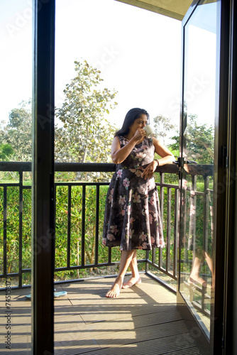 Love for coffee. Portrait of Indian lady drinking enjoying her tea on the balcony over outside terrace with green bush background