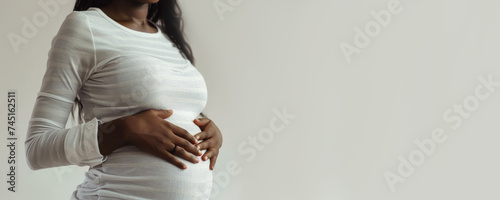 banner pregnant black woman in white clothes holds hands on belly on a white background. Pregnancy, maternity, preparation and expectation. side view. Close-up, copy space.