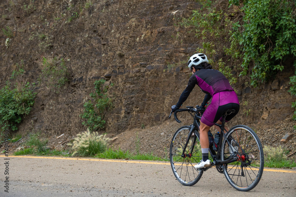 Fototapeta premium athletic female cyclist riding racing bike in competition, dressed in cycling clothes, helmet and gloves. Mountain route