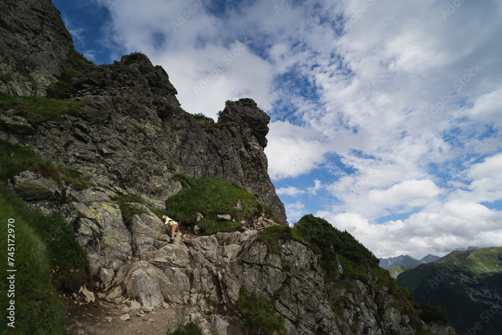 Mountain landscape in the Polish Tatras. A girl traveler climbs a rock.