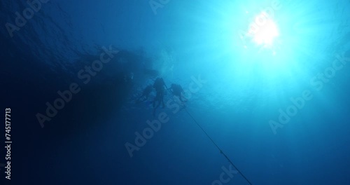 scuba divers safety stop and ascending surface going back to boat underwater with sun beams and rays ocean scenery deco stop photo