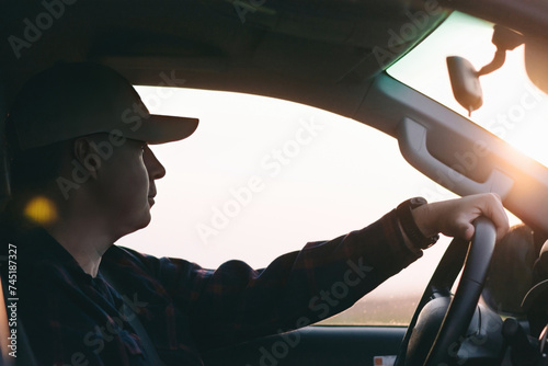 A man is seen driving a car with the sun shining through the windshield. photo