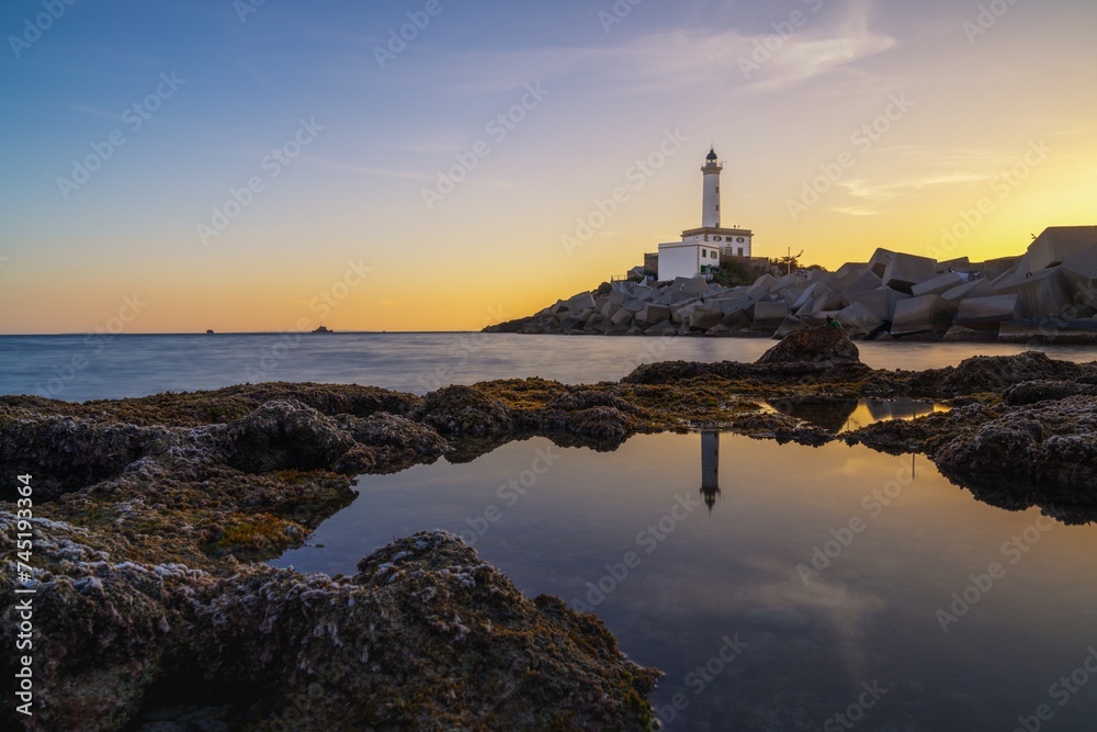 landscape view of the Botafoc Lighthouse in Ibiza Town Port at sunsetwith reflections in tidal pools in the foreground