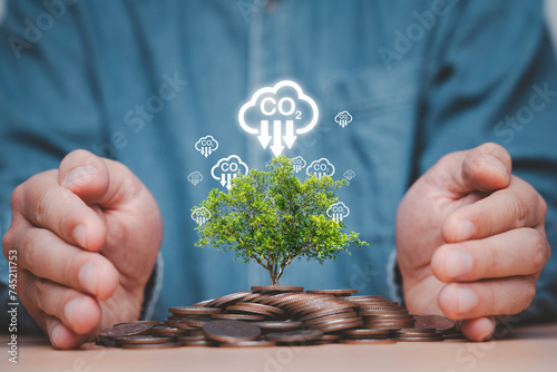 Businessman hand protecting heap of coins and tree with carbon reduction icon for decrease CO2 , carbon footprint and carbon credit to limit global warming from climate change and circular economy.