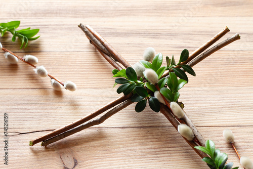 Cross made of branches decorated with boxwood twigs and catkins on wooden background. Creative easter religious concept