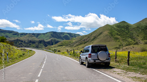 Off-road 4x4 car on a tarmac road in Mtkvari river valley in Samtskhe Javakheti region in Southern Georgia, green grasslands and Caucasus mountains in the background.