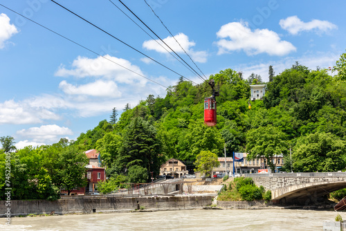 Kutaisi red cable car over Rioni river, lush green trees, residential houses and Upper station in the background. photo