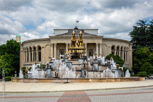 Colchis Fountain in Kutaisi, Georgia, modern fountain with golden statues of animals, replicas of ancient Georgian figures and Meskhishvili Theatre building in the background, symmetrical view photo