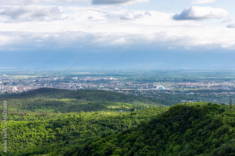 Kutaisi cityscape seen from Sataplia Nature Reserve with Former Georgian Parliament Building and green hills and Colchis forests around, summer, Georgia.