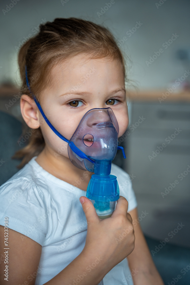 smiling little girl are sitting and holding a nebulizer mask leaning against the face, airway treatment concept