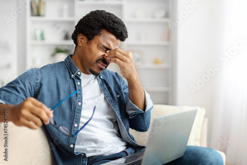 Tired black man rubbing eyes, showing signs of fatigue after using laptop photo