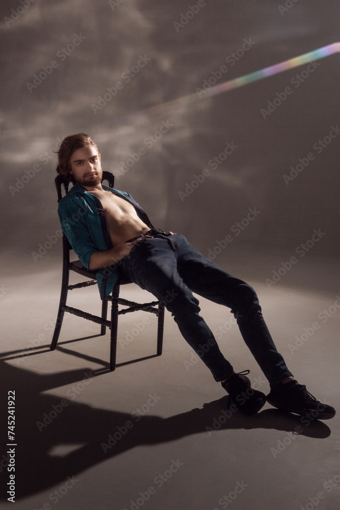A young guy with a beard and an interesting hairstyle sitting lounging on a chair