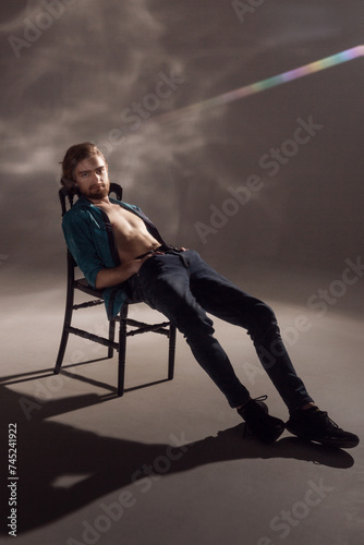 Fototapeta Naklejka Na Ścianę i Meble -  A young guy with a beard and an interesting hairstyle sitting lounging on a chair