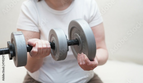 a close-up of women's hands is weighted by dumbbells made of plastic for sports and figure correction of a European woman in a white T-shirt, the concept of sports and an active image