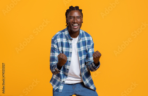 Cheerful young black guy celebrating success on yellow studio background