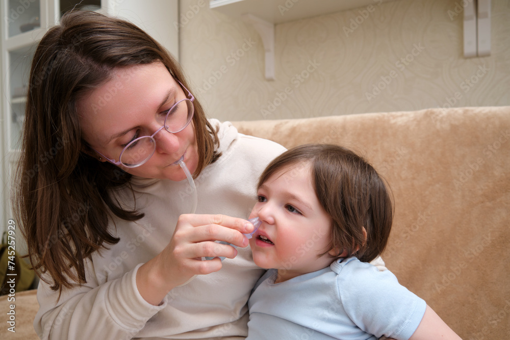 Woman mother using an aspirator to clear snot from baby's nose