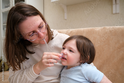 Woman mother using an aspirator to clear snot from baby s nose