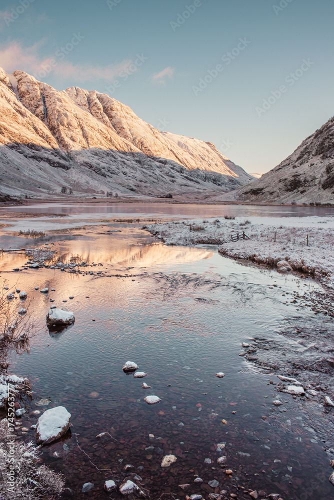 Snow-covered mountains in Glencoe reflect in the waters of Loch Achtriochtan in the Scottish Highlands