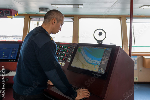 Officer on watch with electronic chart on the navigational bridge. Caucasian man in blue uniform sweater using ECDIS on the bridge of cargo ship.