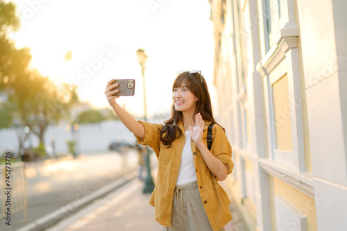 Traveler asian woman in her 30s making a livestream and sefie with a smartphone enjoying travel in Bangkok, Thailand. Journey trip lifestyle, world travel explorer or Asia summer tourism concept. photo