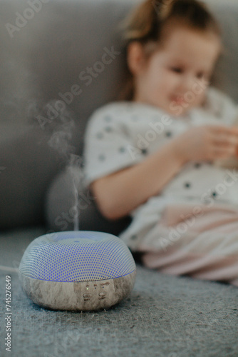 little girl holding bare feet close up to camera and watching phone . Blurred face on background. Diffuser with essential oil 