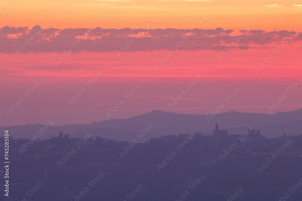 pink sunrise sky with the silhouette of an italian village on the top of a hill in Piedmont