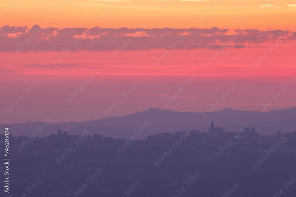 Fototapeta premium pink sunrise sky with the silhouette of an italian village on the top of a hill in Piedmont