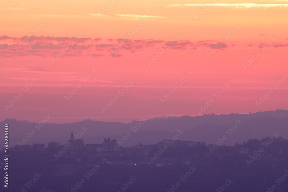 pink sunrise sky with the silhouette of an italian village on the top of a hill in Piedmont