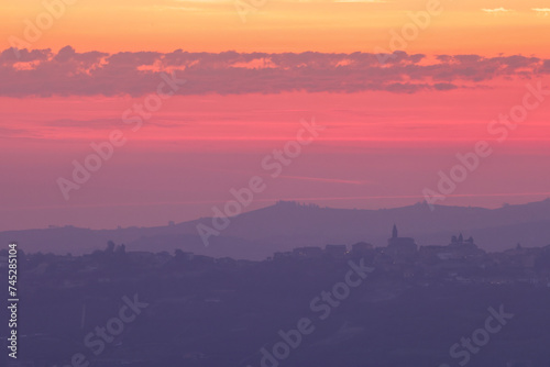 pink sunrise sky with the silhouette of an italian village on the top of a hill in Piedmont