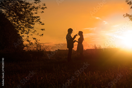 Silhouette of a couple standing in a wheat field at sunset with the man touching the woman's nose, Hungary photo