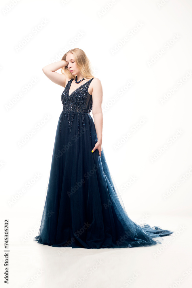 Young blonde woman in a dark blue ball gown with a fluffy skirt on a white background. Young blonde woman in a dark blue ball gown with a fluffy skirt on a white background.