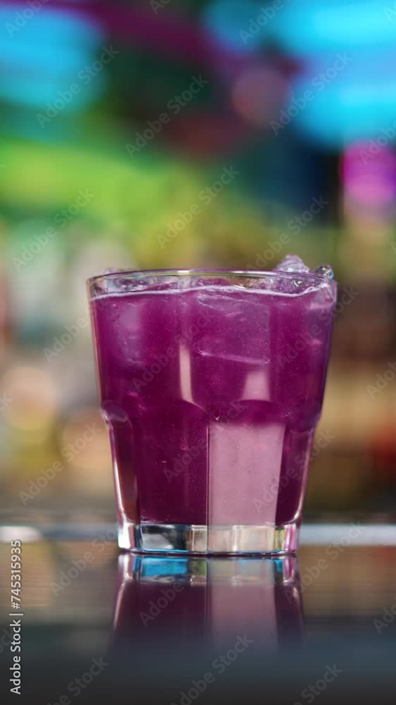 a glass with a beautiful purple cocktail with ice is on the bar counter in a bar or nightclub vertical video a glass with a beautiful purple cocktail with ice is on the bar counter in a bar or nightclub vertical video