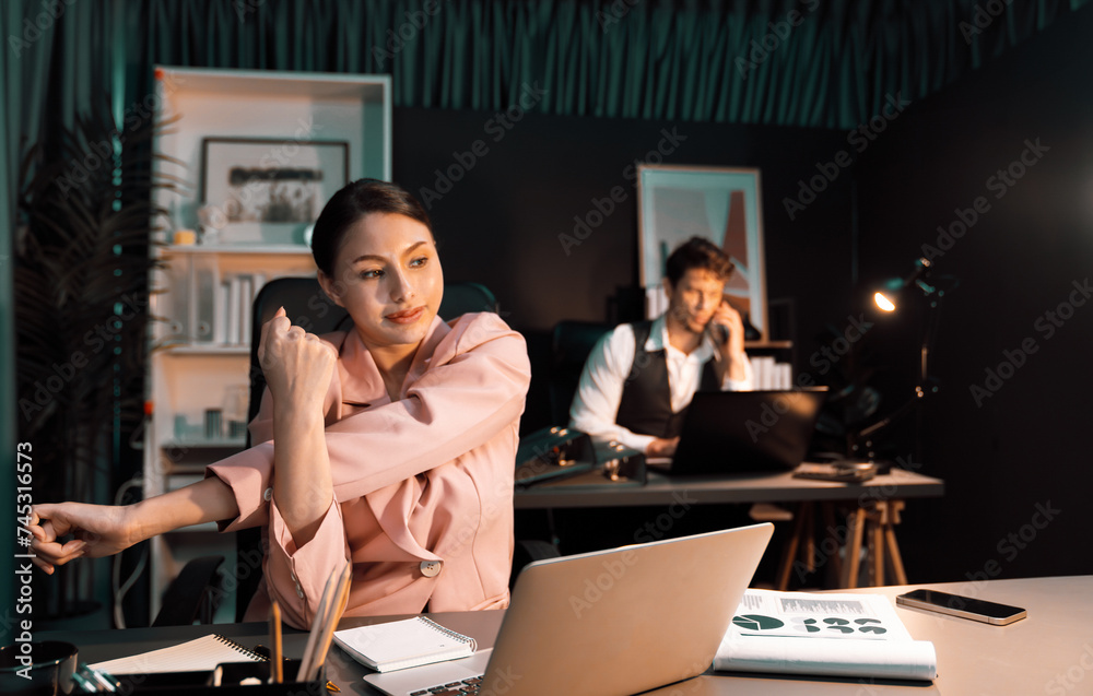 Smart businesswoman having aches with body in back, neck and whole body, stretching composition in long time with man working at blurry back site at neon dark room at late overnight time. Postulate.
