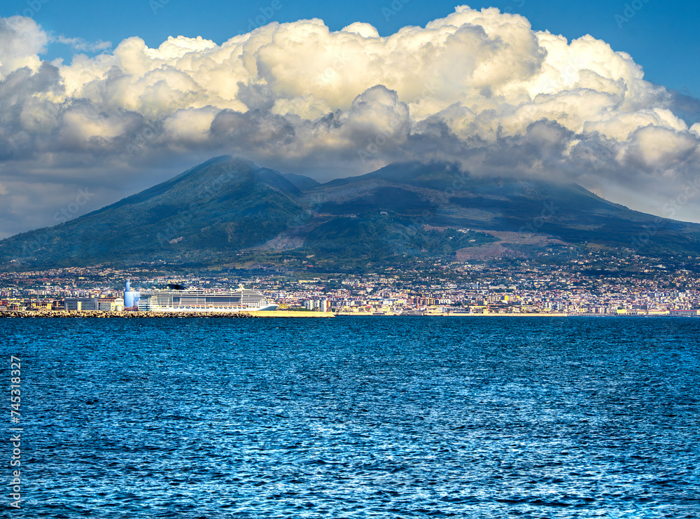 the blue sea of the Bay of Naples with cruise ship at the foot of the volcano Vesuvius overhung by vaporous scenic clouds