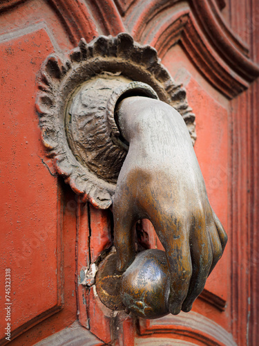 Aldaba, llamador, picaporte antiguo con forma de mano sosteniendo una manzana, en una puerta de época de madera pintada en rojo suave photo