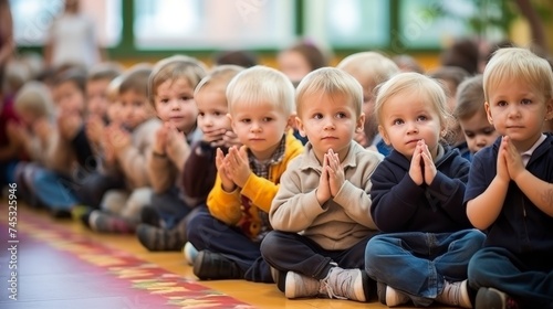 Diverse group of happy small children clapping sitting on floor in a nursery school classroom