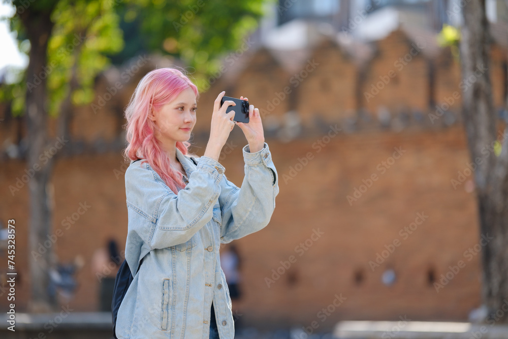 Young woman with long pink hair photographing among the city.