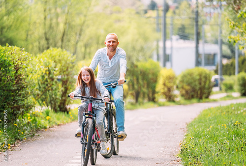 Fototapeta Naklejka Na Ścianę i Meble -  Portraits Smiling father with daughter during summer outdoor bicycle riding. They enjoy togetherness in the summer city park. Happy parenthood and childhood or active sport life concept image.