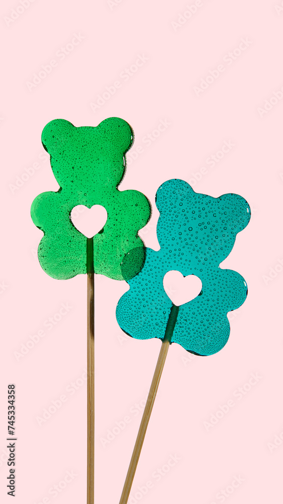 Two transparent lollipops in the shape of bears with a heart on a pink background. Sweet love. Vertical banner for Valentine's Day. Two transparent lollipops in the shape of bears with a heart on a pink background. Sweet love. Vertical banner for Valentine's Day.