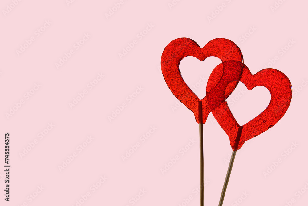 Two red heart-shaped lollipops on a pink background. The word is love. Horizontal banner for Valentine's Day.