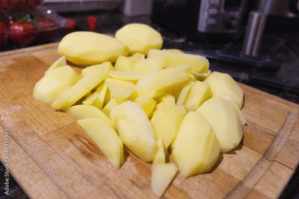 Raw sliced potatoes on a wooden cutting board ready to cook at home kitchen close-up food photo with copy space. Cooking at home, homemade food. Vegetarian or vegan diet. Raw sliced potatoes on a wooden cutting board ready to cook at home kitchen close-up food photo with copy space. Cooking at home, homemade food. Vegetarian or vegan diet.