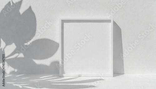 Light monochrome wall with square mockup and white frame. On the left are soft shadows from the leaves