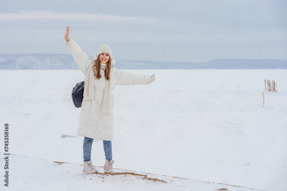 Winter photo of a young girl in a white jacket and with a backpack walking through snow and ice on a frozen river, snowy desert landscape