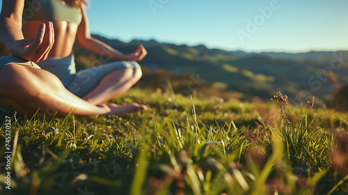 Mulher praticando yoga em colina gramada com céu azul e montanhas ao fundo photo
